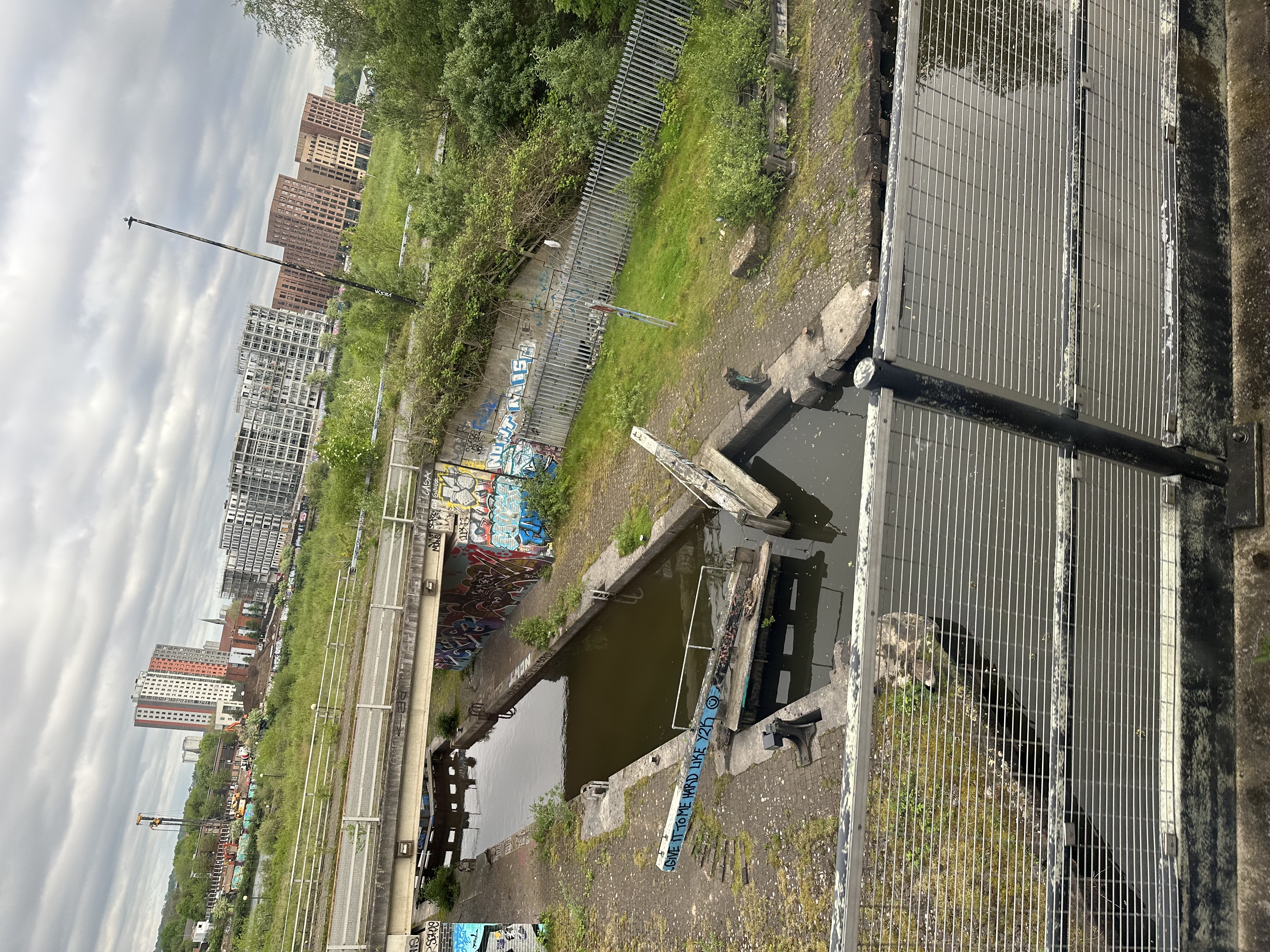 View on manchester over a river, as seen from the tram. On a sluice gate graffity says:'give it to me hard like Y2K'.